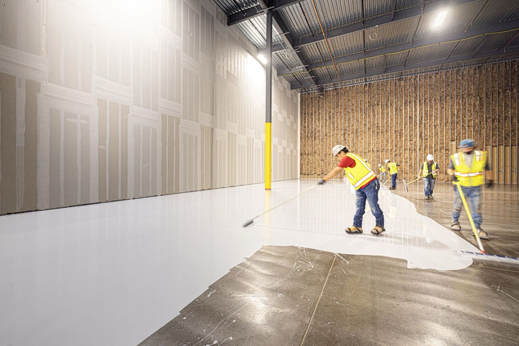 A crew in hard hats and high-visibility vests working a fresh concrete floor.