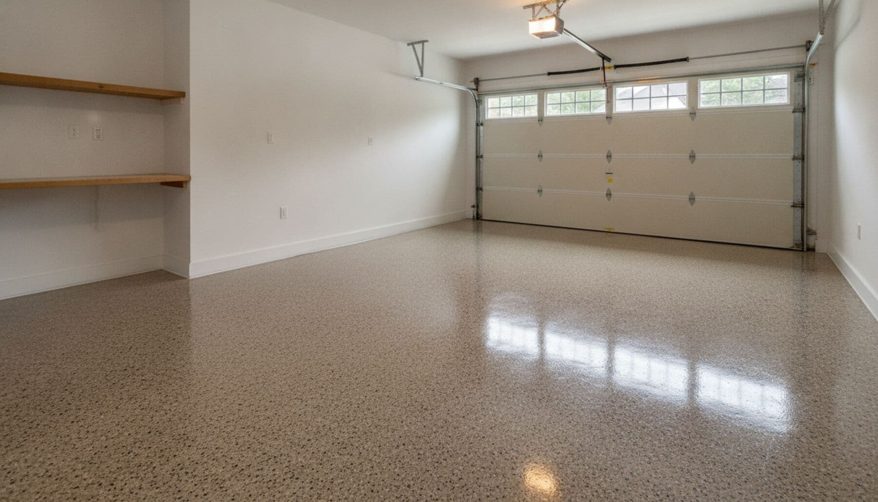 A residential two-car garage with a freshly installed flake epoxy floor coating in warm grey, reflecting the daylight.