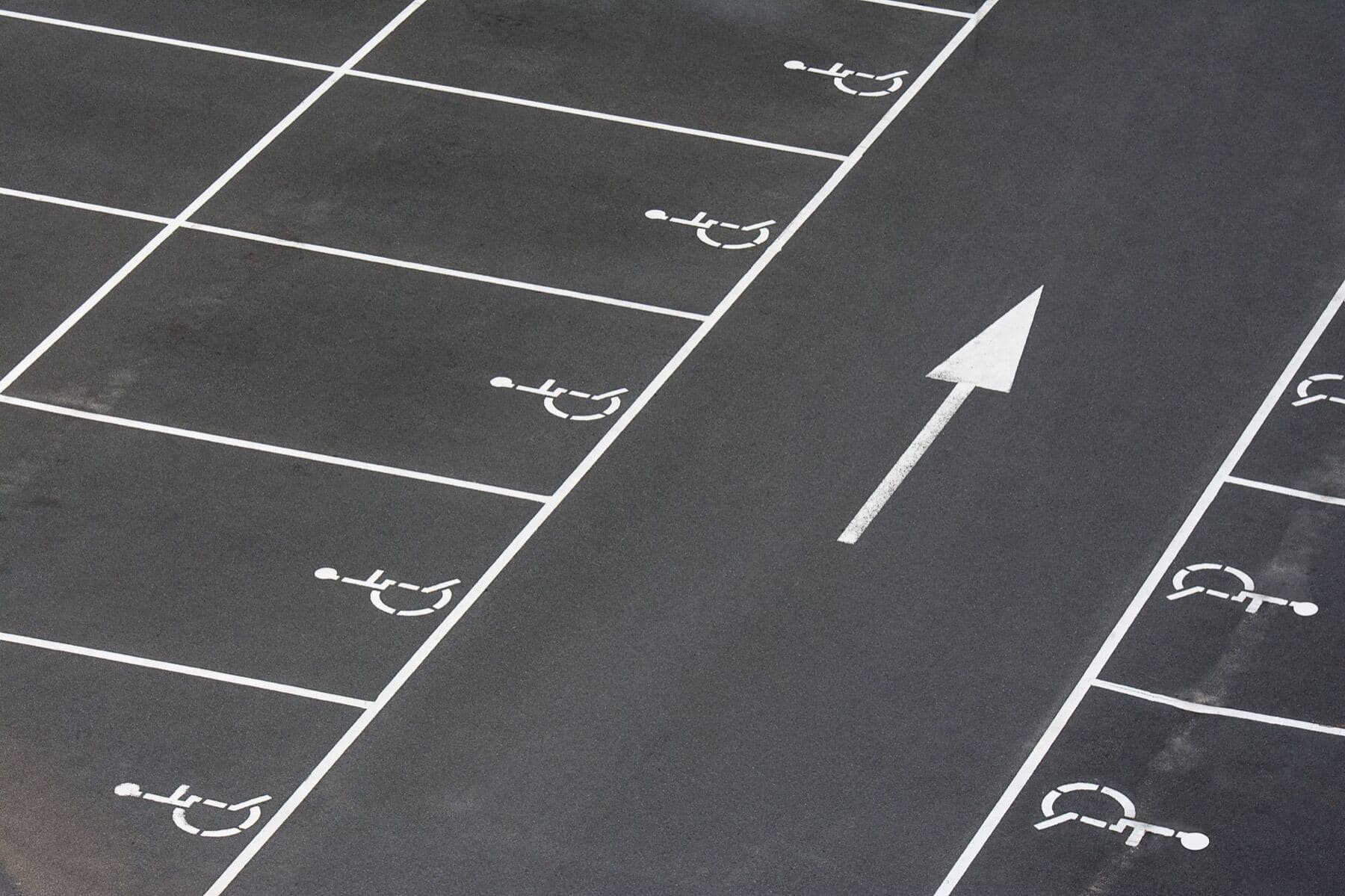 A parking lot with freshly painted stall lines, an accessible stall symbol and a directional arrow.